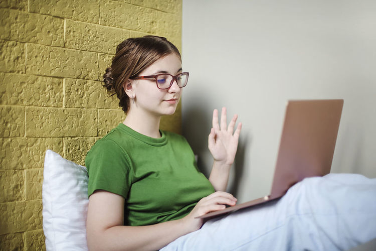 Midsection of woman using mobile phone while sitting on bed against wall