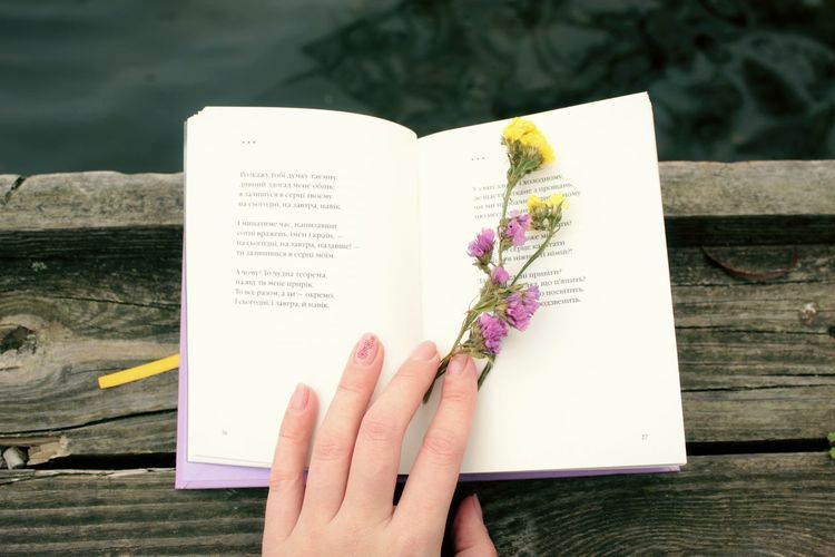 Cropped image of hand holding book against white wall
