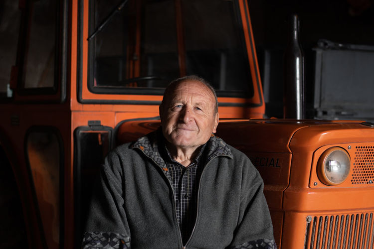Portrait of senior man sitting by vehicle outdoors