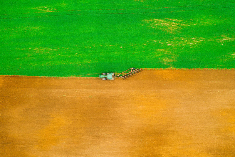 Aerial photo of brown and green field. tractor harrows the ground. horizontal pattern.