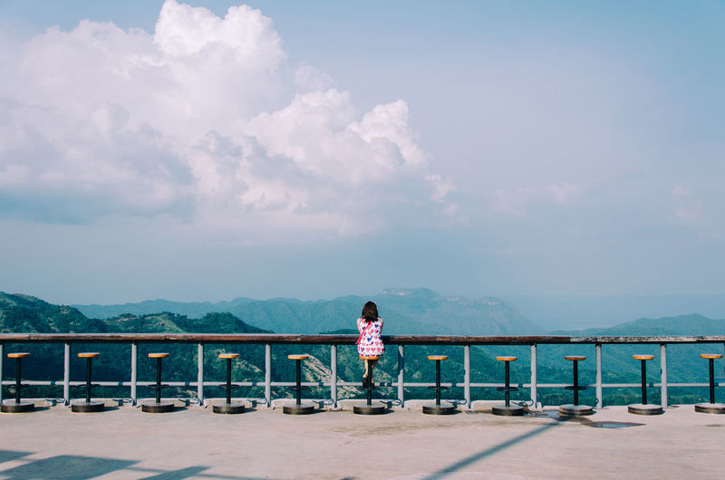 Woman sitting by railing against sky