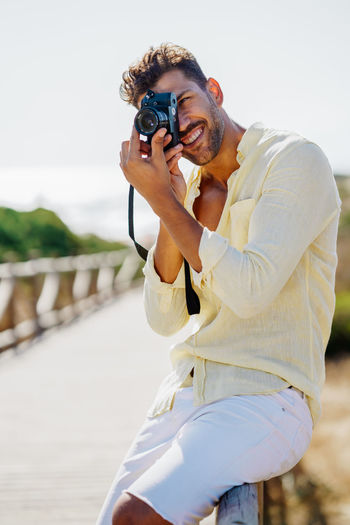 Smiling man with camera photographing while standing by railing