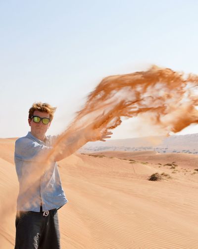 Portrait of man throwing sand against clear sky