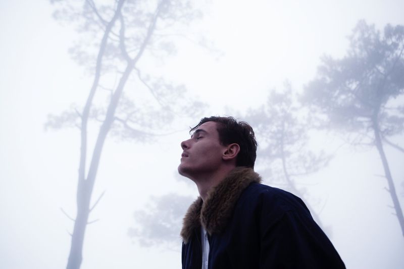 Low angle view of thoughtful man standing in forest during foggy weather