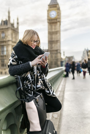 Uk, london, young woman using her smartphone on westminster bridge