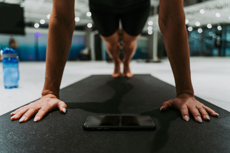 Low section of young woman exercising on mat with mobile phone at gym