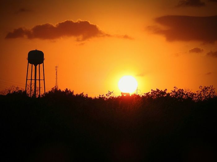 Silhouette plants and water tower against orange sky during sunset