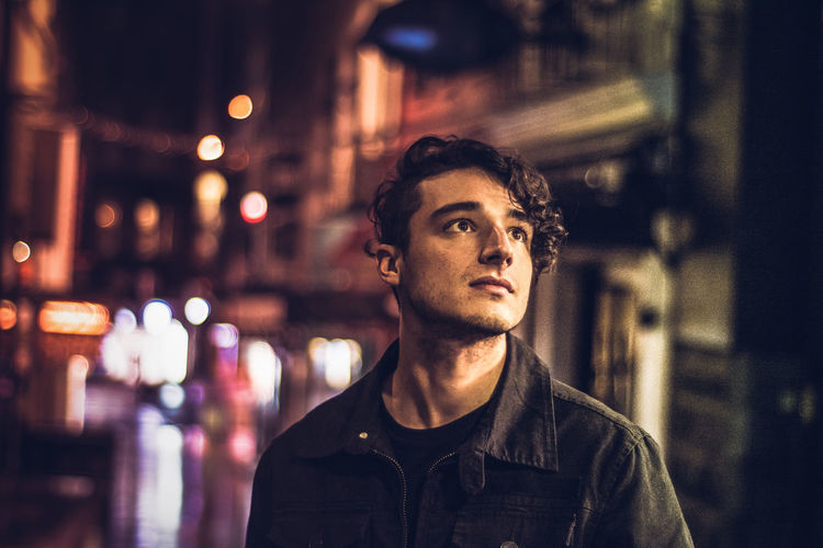 Portrait of young man looking away in city at night