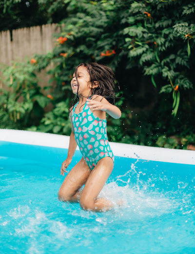 Diverse mixed race toddler girl at home having fun in kiddie pool in backyard being very happy