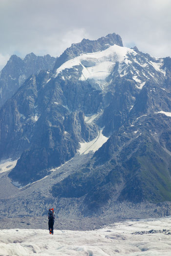 Rear view of hiker walking against snowcapped mountain