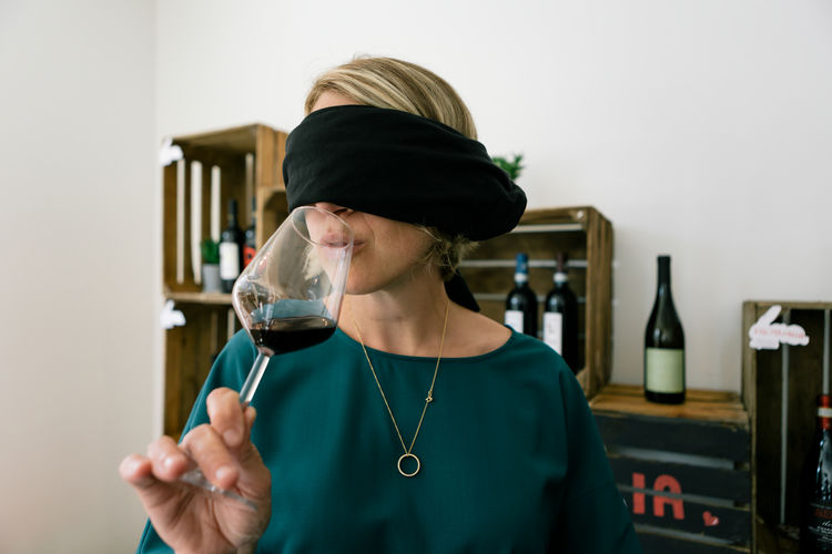 Woman with covered eyes doing wine drink degustation inside bar restaurant - face wearing blindfold