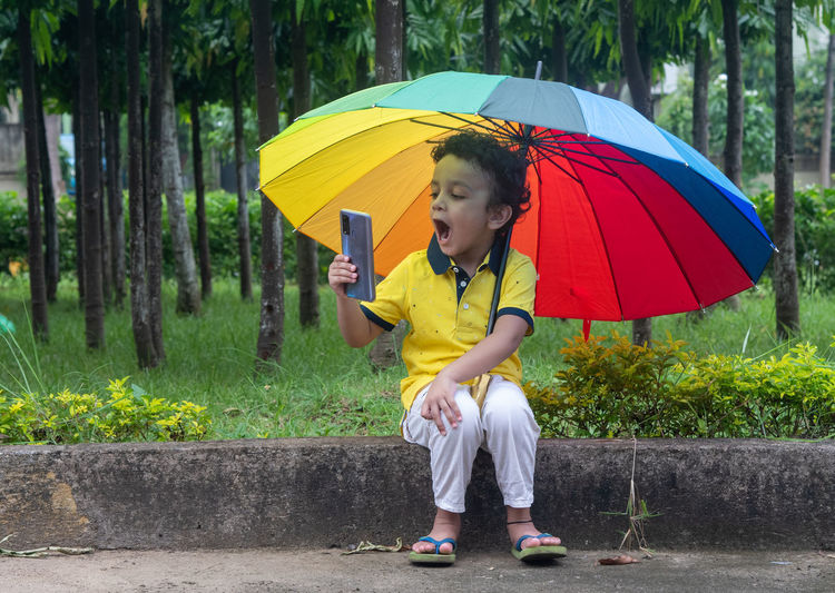 Full length of boy holding multicolored umbrella on rainy day