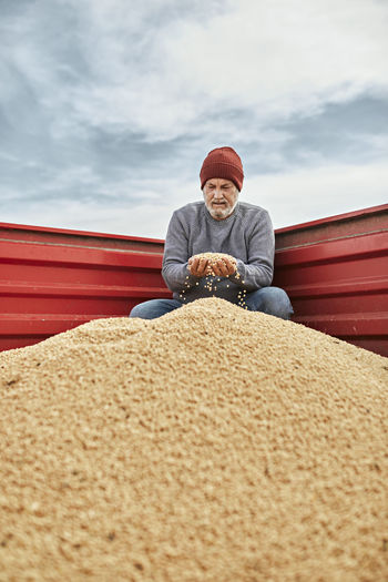 Farmer holding soybean in hand while sitting in tractor against sky