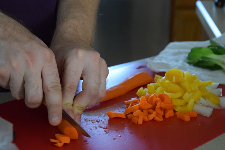 Midsection of man cutting carrots on red cutting board in kitchen