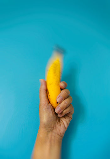Cropped hand of man holding banana against blue background