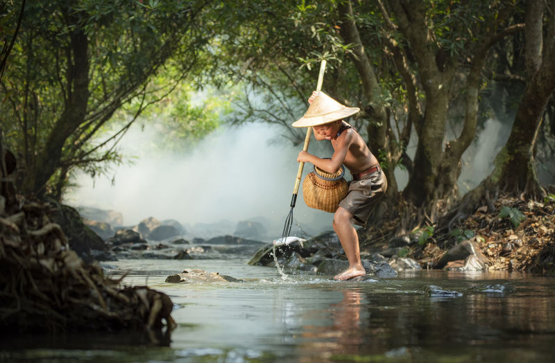 Boy catching fish while standing by river in forest
