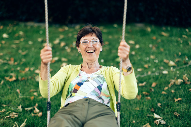 Positive smiling healthy elderly woman plays on the swing