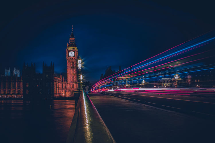 Light trails on road amidst buildings against sky at night