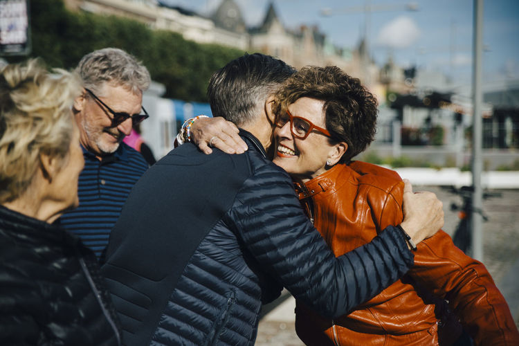 Happy senior woman embracing man by friends in city during vacation