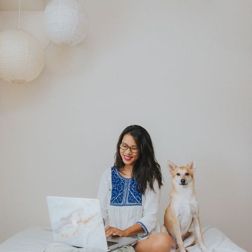Smiling woman using laptop while sitting dog at home