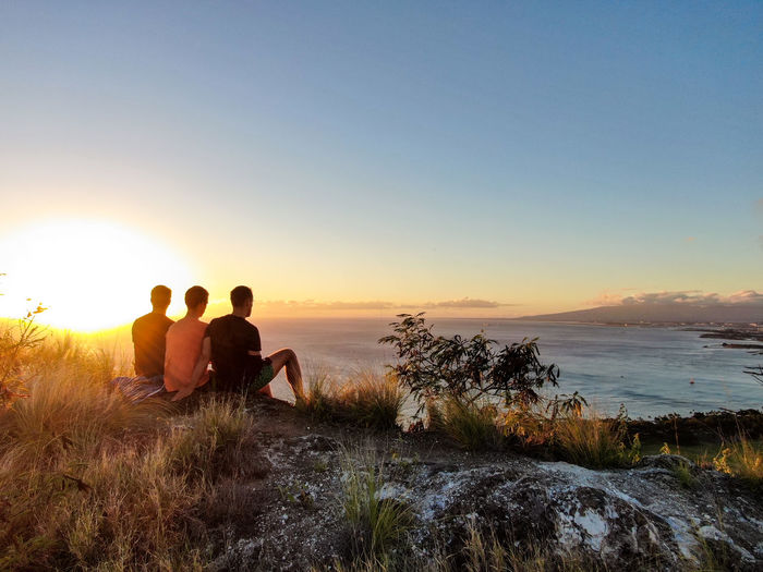 Rear view of friends looking at sea from peak against sky during sunset