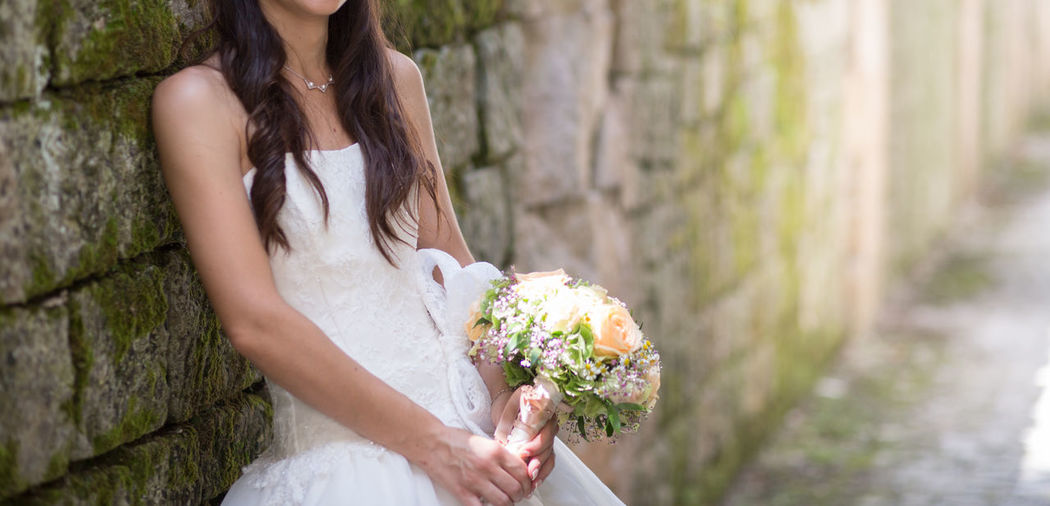 Bride with bouquet leaning on wall