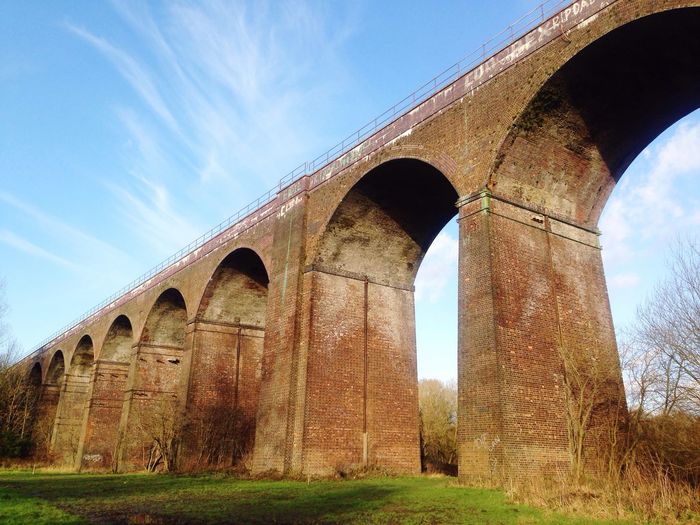 Low angle view of historic bridge over field against sky