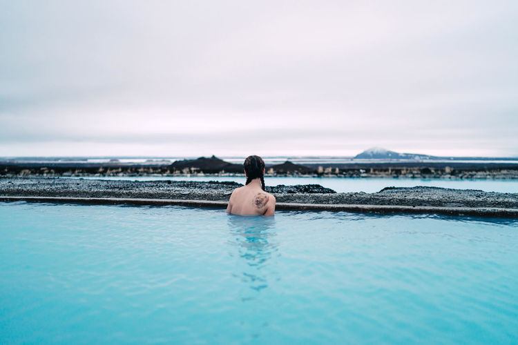 Rear view of woman swimming in infinity pool against sea