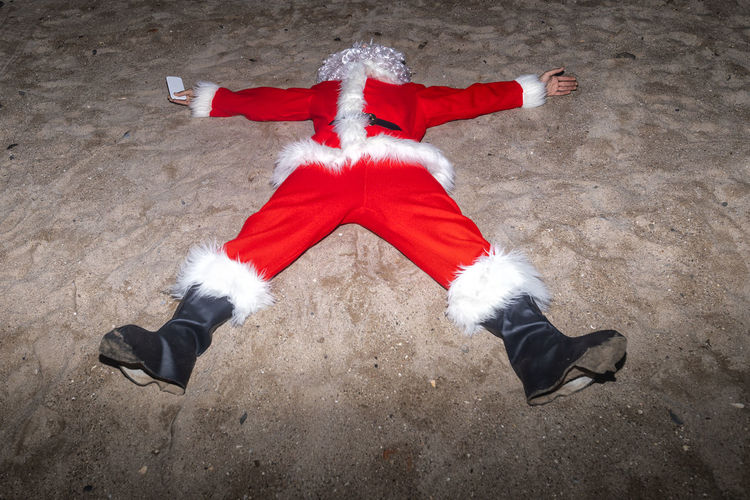 Man wearing santa claus costume lying on sand at beach