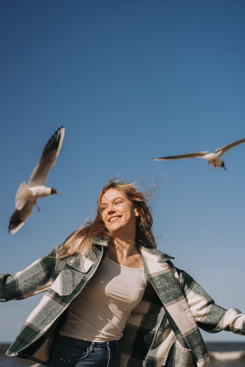 Happy young woman dancing near the sea. seagulls flying on background