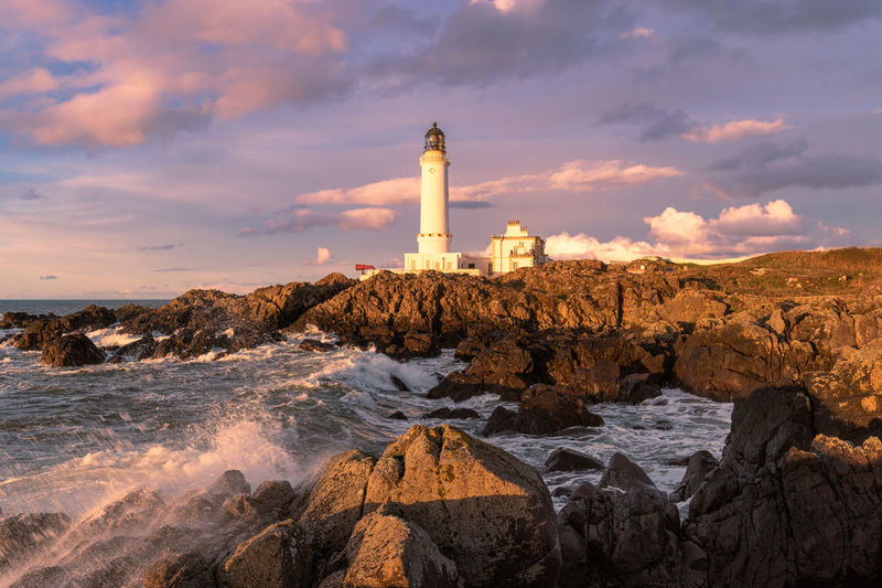 Lighthouse on rocks by sea against sky