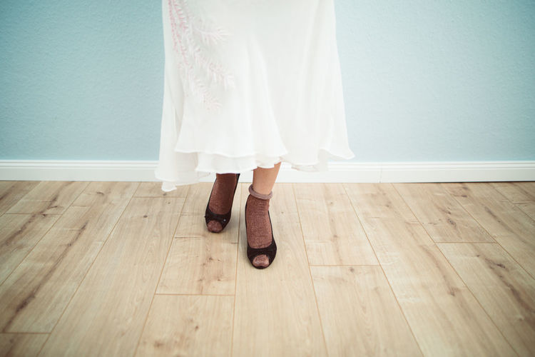Low section of woman wearing high heels while standing on hardwood floor