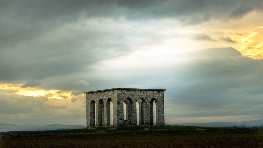 Old structure on field against cloudy sky during sunset