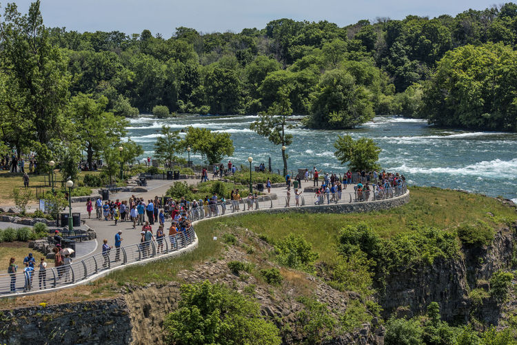 People by boats in river against trees