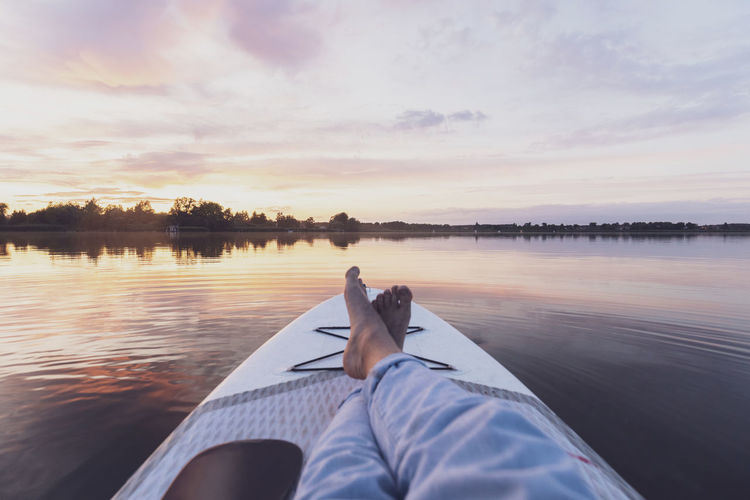 Legs of woman relaxing on paddleboard during sunset