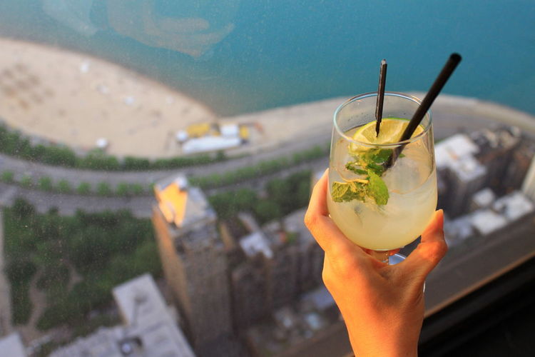 Cropped hand of woman holding drink over cityscape