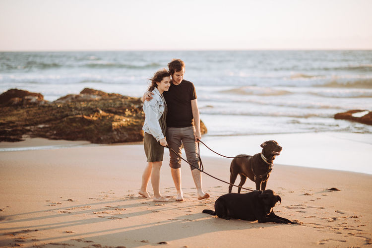 Wide angle view of millennial couple standing with dogs on shore