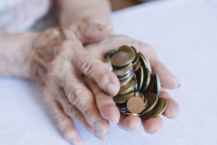 Wrinkled hands of senior woman holding coins