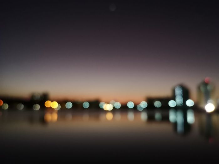 Defocused image of illuminated city by sea against sky at night
