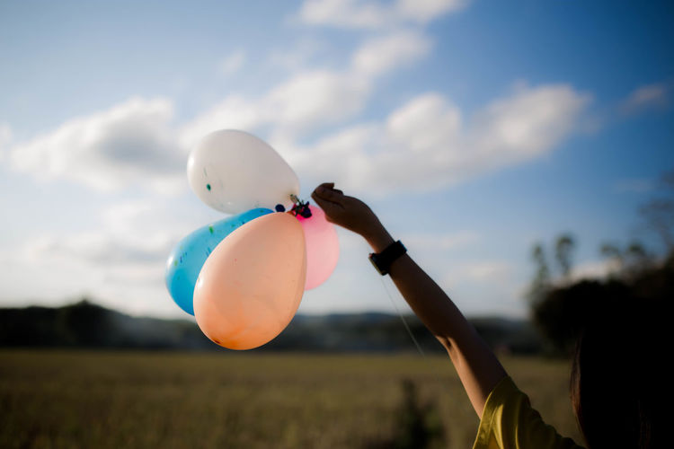 Rear view of woman holding balloons on field against sky