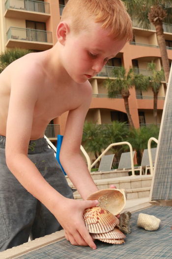Shirtless boy holding shells against building