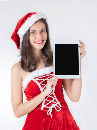 Portrait of smiling young woman holding smart phone while standing against white background