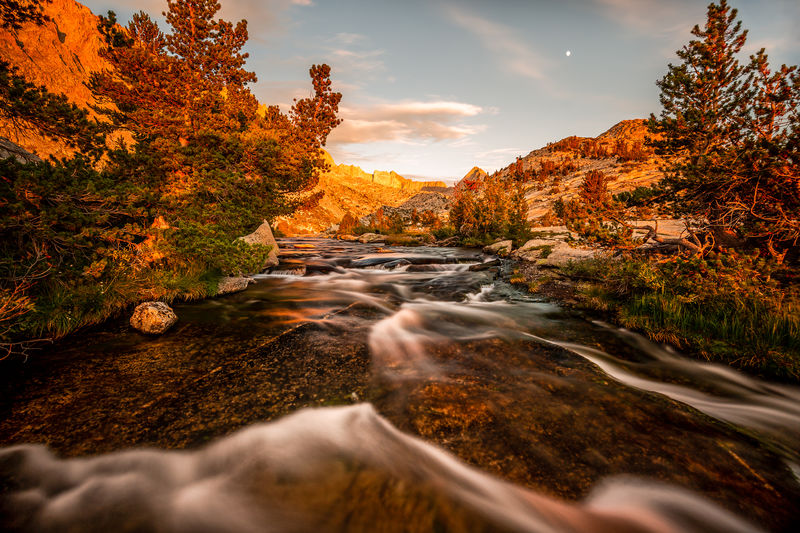 Surface level of stream flowing through rocks against sky during sunset