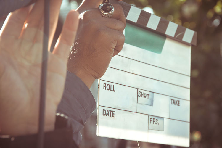 Cropped hand of man holding film slate while standing outdoors