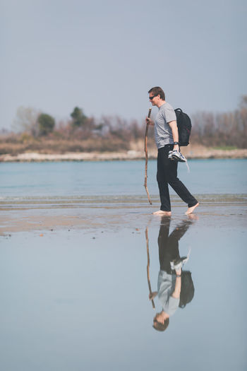 Full length side view of man with stick walking on shore at beach