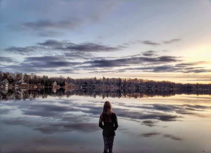 Woman standing by lake landscape during sunset