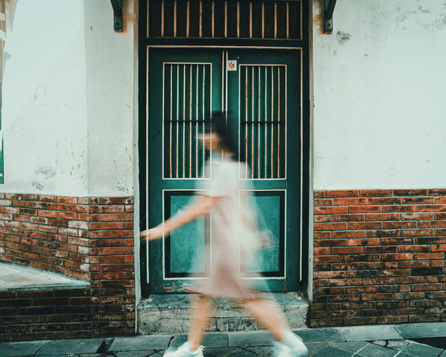 Blurred motion of woman walking against building