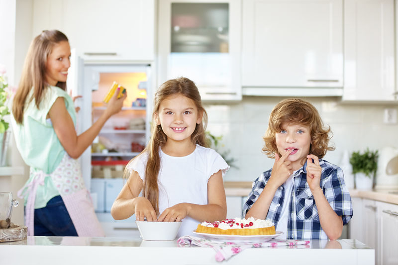 Mother looking at children making cake in kitchen at home