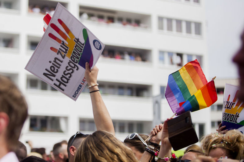 Cropped image of people with placard with multi colored flag during gay parade