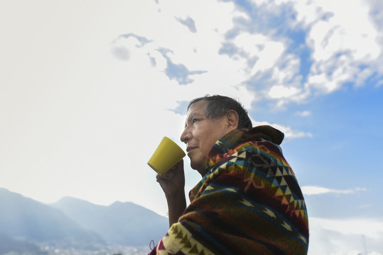 Man wearing traditional poncho looking away while drinking coffee